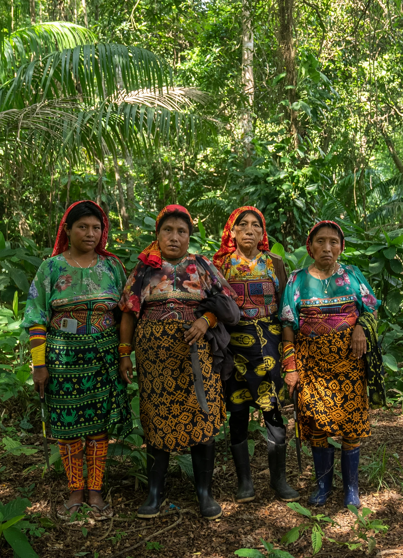Four Guna women in traditional dress standing in a tropical forest with machetes