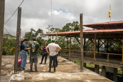 People talking on a rooftop terrace beside a bamboo pavilion with a red metal roof