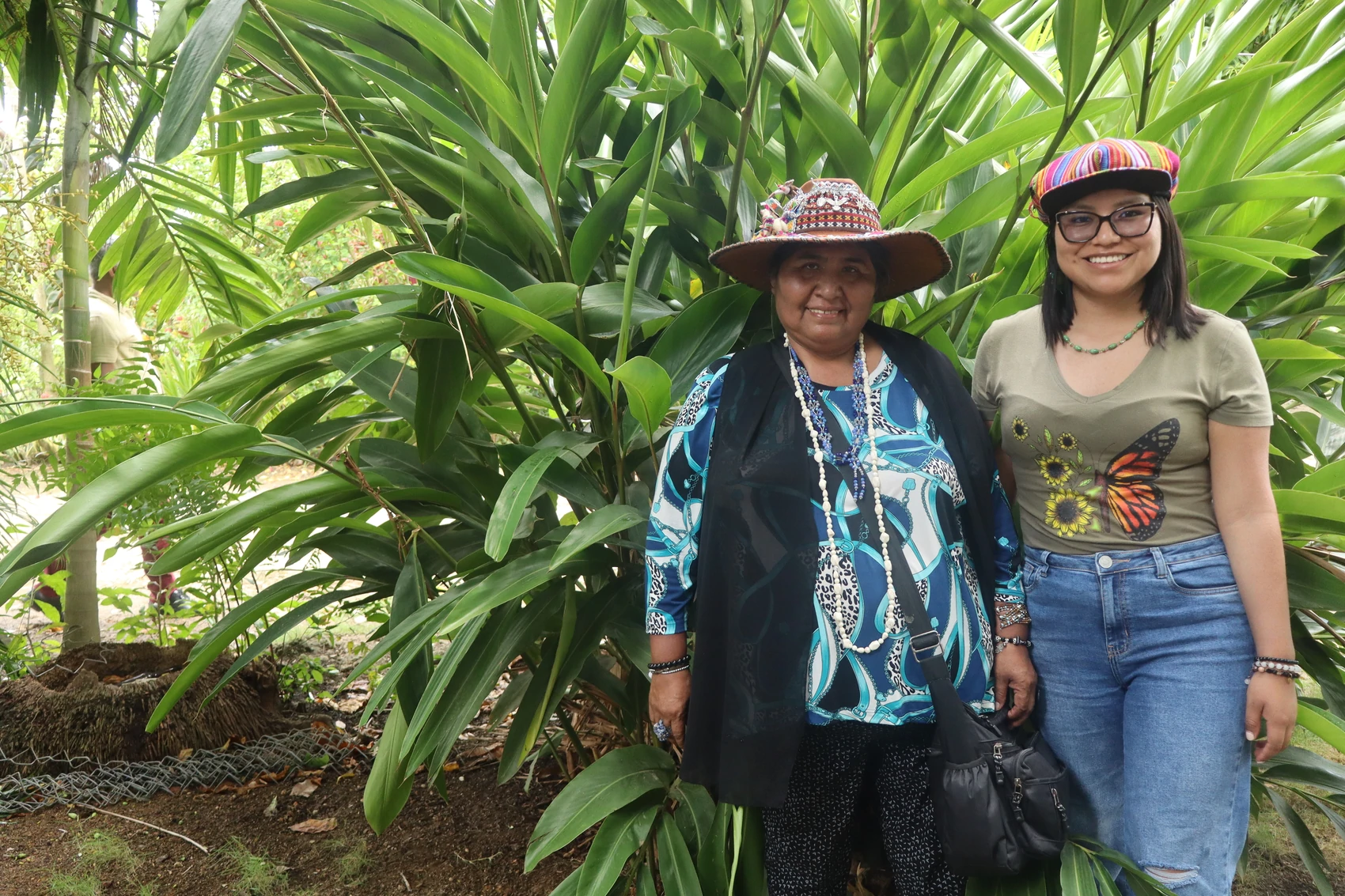 Two women smiling together in front of dense tropical foliage