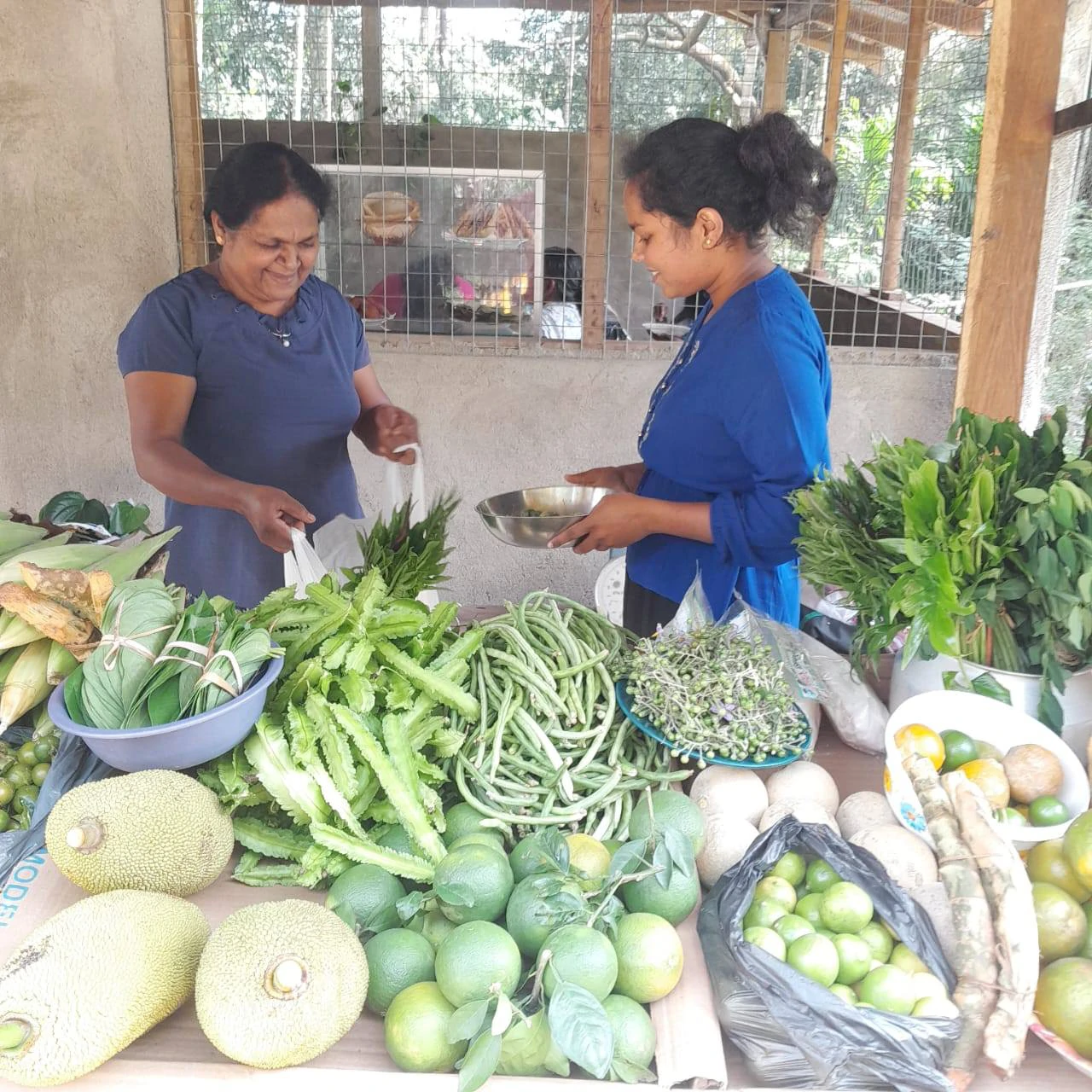 Two women smiling at a market stall filled with fresh tropical produce