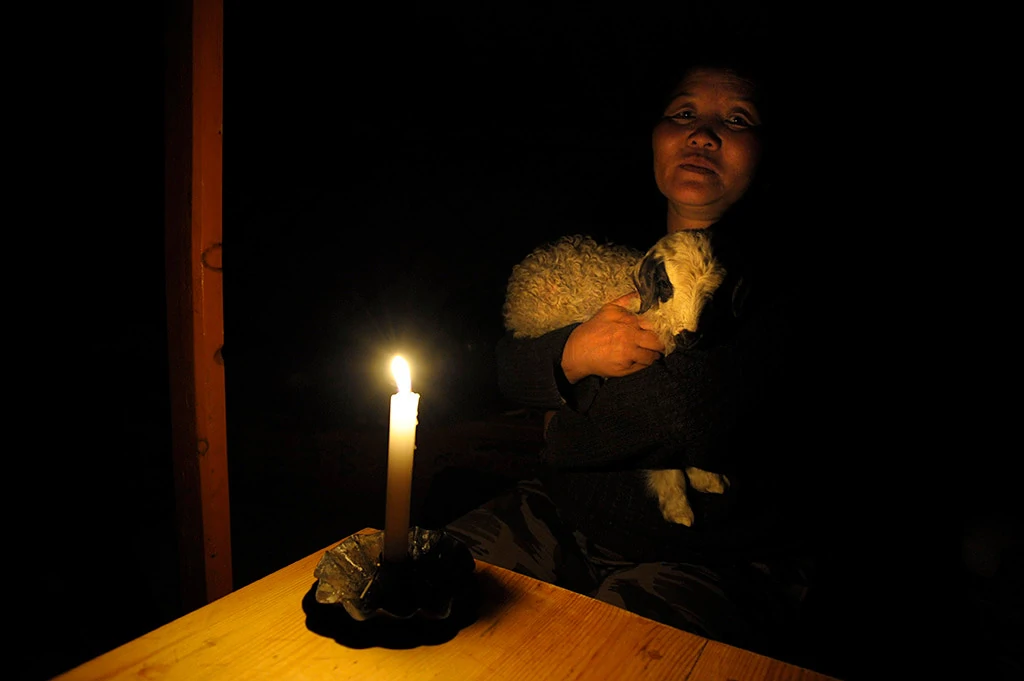 Woman cradling a lamb by candlelight in a dark room