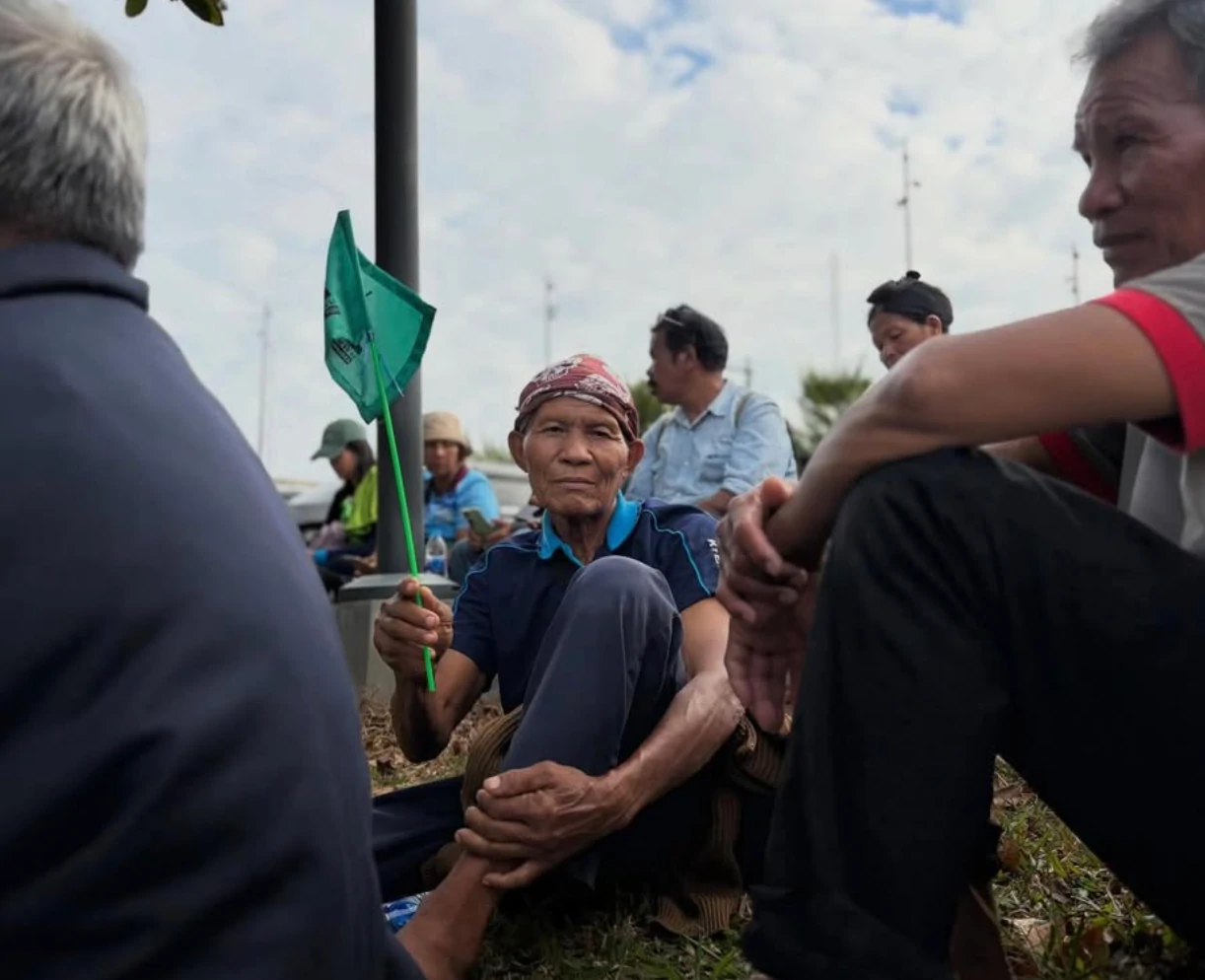 Elderly man sitting on the grass holding a small green flag at an outdoor gathering