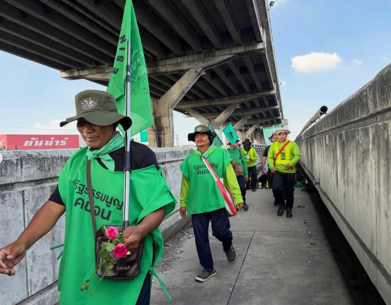 People marching under a highway overpass wearing green tunics and carrying green flags