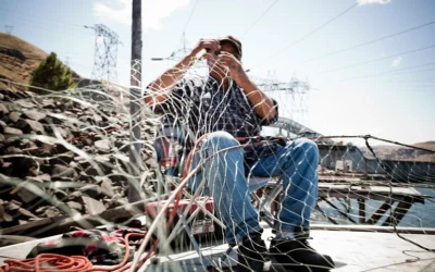 Man repairing a fishing net on a wooden dock with power lines in the background