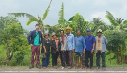 Representatives of the Assembly of the Poor movement in Thailand standing with a foreign visitor in front of agricultural fields.