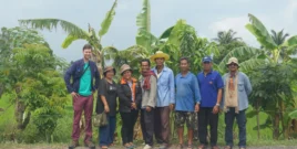 Representatives of the Assembly of the Poor movement in Thailand standing with a foreign visitor in front of agricultural fields.
