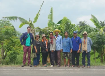 Representatives of the Assembly of the Poor movement in Thailand standing with a foreign visitor in front of agricultural fields.