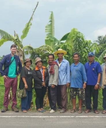 Representatives of the Assembly of the Poor movement in Thailand standing with a foreign visitor in front of agricultural fields.
