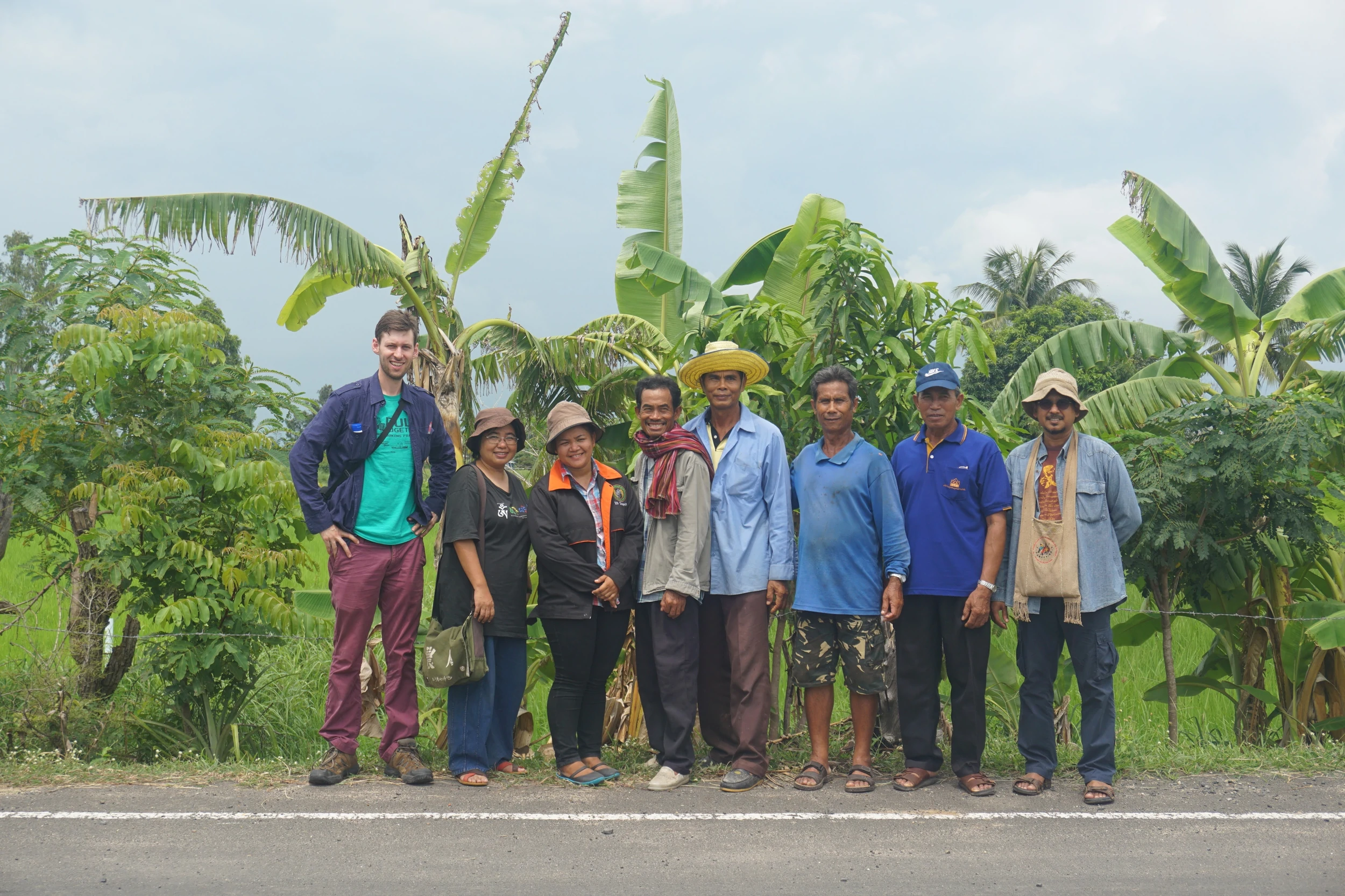 Representatives of the Assembly of the Poor movement in Thailand standing with a foreign visitor in front of agricultural fields.