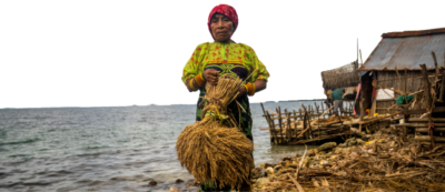 Guna woman in traditional dress holding a harvest bundle by the shore