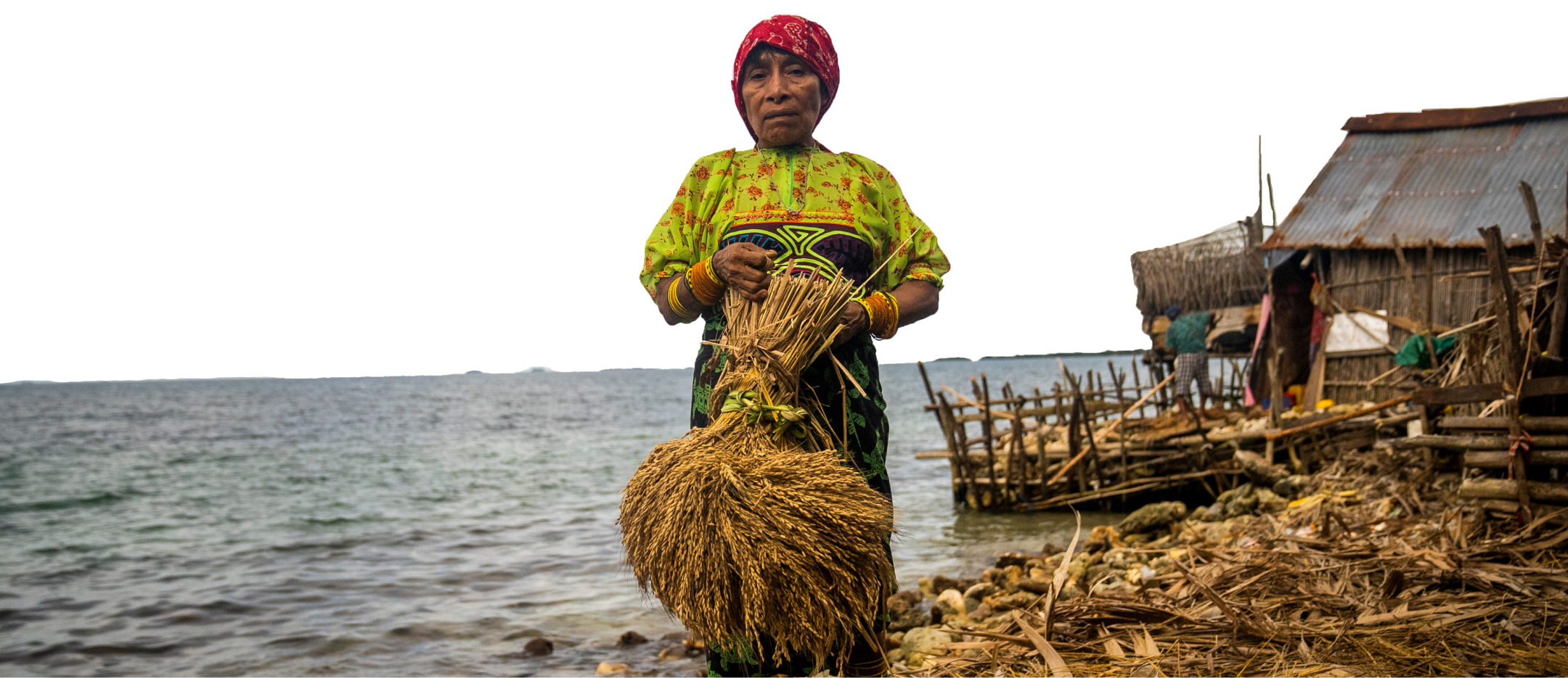 Guna woman in traditional dress holding a harvest bundle by the shore
